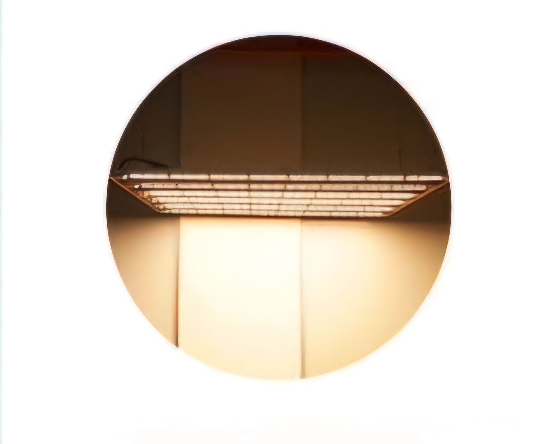 Circular mirror with reflection of a shelf and soft lighting in a minimalistic setting.